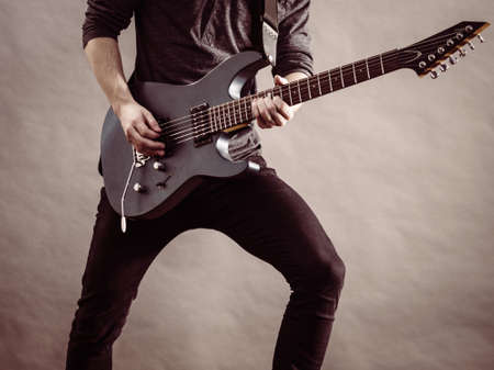 Unrecognizable male person with electric guitar. Close up, part body guy is holding instrument and...