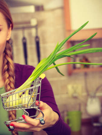 Buying healthy dieting food concept. Woman in kitchen having many green vegetables holding small shopping cart trolley with chive inside.の写真素材