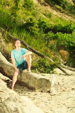 Summertime relaxation, vacation and holiday, adventure traveling concept. Handsome man sitting on tree trunk relaxing during summer.の写真素材