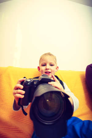 Child passion and hobbies concept. Kid playing with big professional digital camera, photographing various things in houseの写真素材