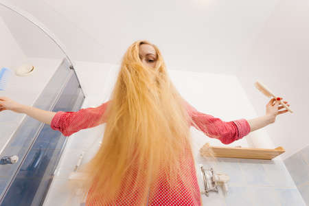 Woman wearing pajamas in bathroom having fun while brushing her long blonde hair, windblown hairdo, shot from bottom.の写真素材
