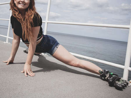 Happy joyful young woman wearing roller skates fooling around stretching her legs. Female being...