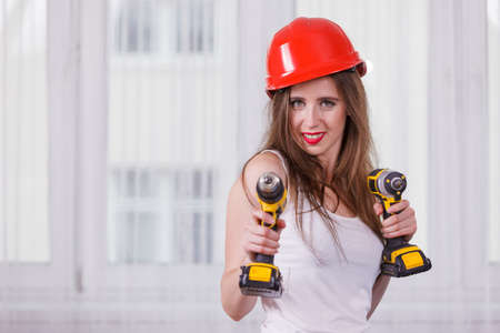 Young positive woman using power driil for work at home. Girl working at flat remodeling. Building,...
