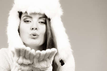 Woman wearing white furry hat sending air kisses. Winter fashion accessories concept.