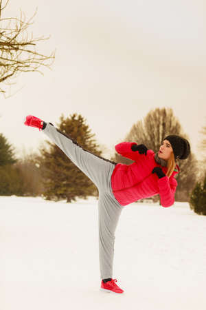 Outdoor sport exercising, sporty outfit ideas. Woman wearing warm sportswear training karate outside during winter.の写真素材