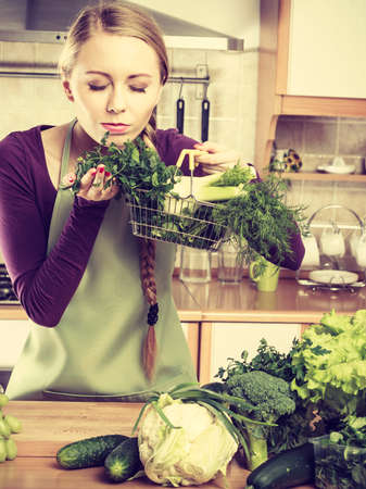 Buying healthy dieting food concept. Woman in kitchen having many green vegetables holding small shopping basket.の写真素材