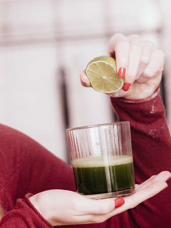 Drinks good for health, diet breakfast concept. Young woman in kitchen holding green healthy vegetable smoothie juice glassの写真素材