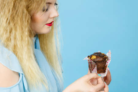 Sweet food sugar make us happy. Attractive blonde woman holds yummy chocolate cupcake in hand, craving for cake. Appetite and tasty meal dessert.の写真素材