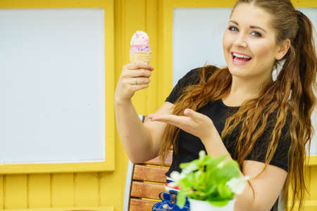 Happy funny young woman with long brown hair eating ice cream having fun.の写真素材