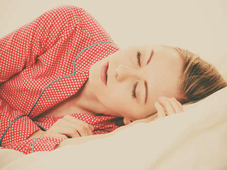 Relax rest sleep positions concept. Girl drowning in dreams. Young woman wearing red dotted pajamas lying in bed on the side dreaming deeply.の写真素材