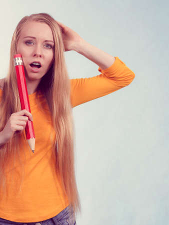 Nervous young blonde teenage girl going to school or college wearing backpack and holding big pencil feeling very stressed outの写真素材