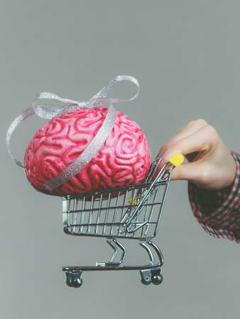 Woman hand holding shopping cart with brain inside. Clever, responsible buying concept.の写真素材