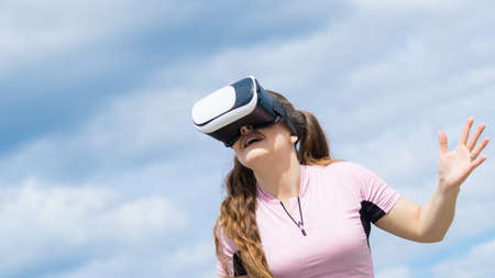 Young woman testing VR glasses outside. Female wearing virtual reality headset during summer weather