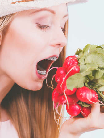 Funny young woman about to bite red delicious radish. Summer vegetables concept.の写真素材