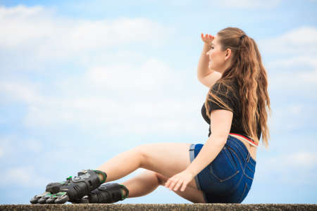 Happy joyful young woman wearing roller skates relaxing after long ride. Female being sporty having fun during summer time near sea.の写真素材