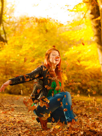 Happiness carefree leisure concept. Redhaired long hair woman relaxing in autumn park throwing leaves up in the air. Beautiful girl in orange forest foliage outdoor.の写真素材