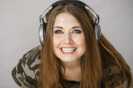 Cheerful teenage woman listening to music through big headphones having fun. Crazy girlの写真素材