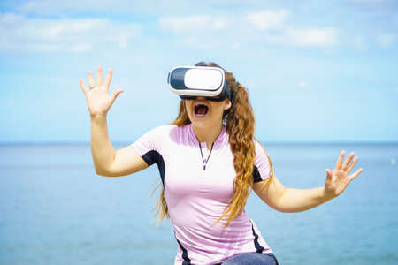 Young woman testing VR glasses outside. Female wearing virtual reality headset during summer weatherの写真素材