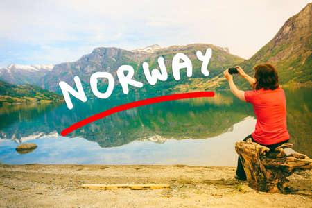 Tourism and travel. Woman tourist taking photo with camera, enjoying mountains lake Oppstrynsvatnet view in Jostedalsbreen National Park, Oppstryn (Stryn), Sogn og Fjordane county. Norway Scandinavia.の写真素材
