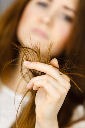 Worried woman looking at her dry split long brown hair ends, thinking of good treatment. Haircare and hairstyling concept.の写真素材