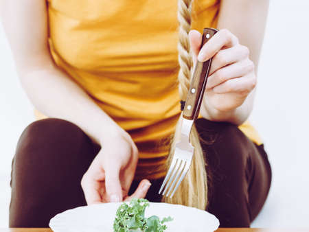 Unrecognizable woman being on diet starving herself holding fork having plate with one piece of lettuce.の写真素材
