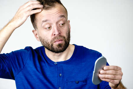 Sad worried man looking at his hair in small pocket mirror being stressed about look.の写真素材
