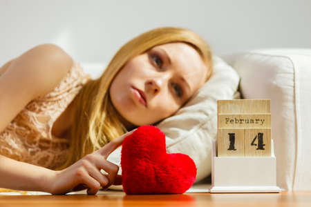 Sad lonely woman lying on bed looking at calendar, 14 Valentines day being alone with heart shape.の写真素材