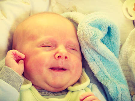 Infant care, beauty of childhood concept. Little newborn baby sleeping calmly in bed surrounded with blankets making funny faces.の写真素材