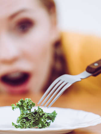 Shocked young blonde woman dealing with anorexia nervosa or builimia having small green vegetable on plate. Dieting problems, eating disorder.の写真素材