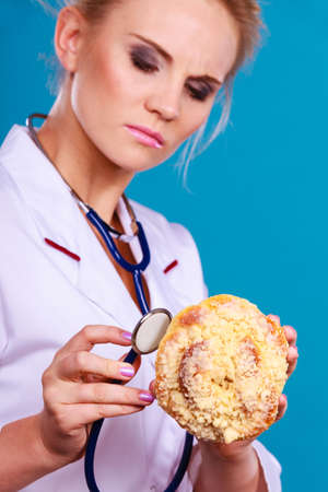 Serious dietitian nutritionist checking examine sweet roll bun with stethoscope. Woman with fattening junk food. Bad unhealthy eating nutrition concept.の写真素材