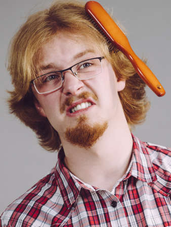 Bearded man having trouble with combing his hair using brush. Male haircare problems concept.
