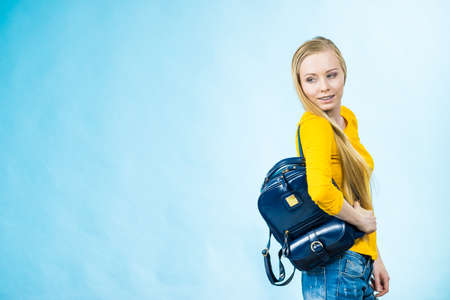 Blonde teenage girl going to school or college wearing stylish backpack. Outfit trendy accessories. On blueの写真素材