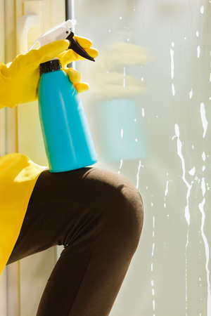 Female hand in yellow gloves cleaning window with blue rag and spray detergent. Spring cleanup, housework conceptの写真素材