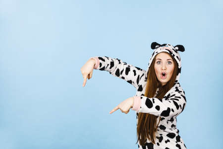 Happy teenage girl in funny nightclothes, pajamas cartoon style pointing down with positive surprised face expression, studio shot on blue. Advertisement conceptの写真素材
