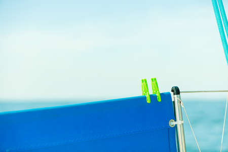 Green plastic clothes clips holding blue heavy fabric on metal string fence, light backgroundの写真素材