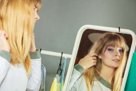 Pretty happy woman in mirror adjusting hair with clothing from new collection wardrobe. Young undecided shopper girl choosing in second hand. Shopping sale concept.の写真素材