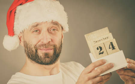 Man wearing santa claus christmas hat holding calendar with 24 december date, studio shot.
