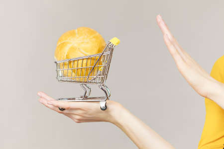 Buying gluten food products concept. Skeptical woman holding shopping cart trolley with bun breal roll showing stop gesture sign.の写真素材