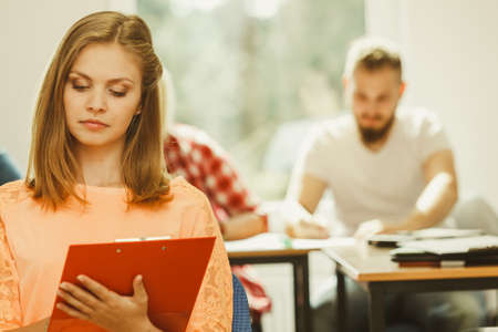 Education, high school, teamwork and people concept - student girl with notebook sitting in front of students her group mates in classroomの写真素材