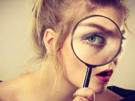 Blonde woman holding magnifying glass investigating something and looking closely, trying to find solution.の写真素材