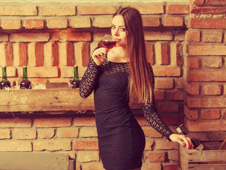 Elegant beauty lady long hair full make up wearing black dress tasting wine in rural cottage interior cellerの写真素材