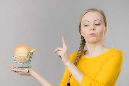 Buying gluten food products concept. Skeptical woman holding shopping cart trolley with bun breal rollの写真素材
