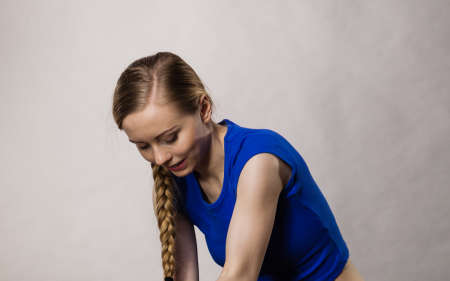 Blonde young woman having braided hairstyle wearing sports wear relaxing after training. Gray background.の写真素材