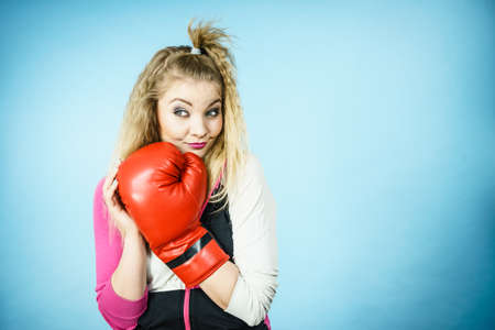 Funny blonde girl female boxer in big fun red gloves playing sports boxing studio shot on blue