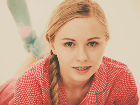 Laziness relax concept. Smiling positive teen girl in bed. Lazy youthful female wearing red dotted pajamas lying on pillow in good mood. Toned imageの写真素材