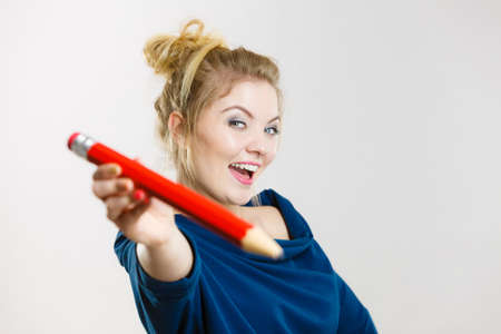 Happy woman holding giving big pencil, school education encouraging. Studio shot on light grey background.の写真素材