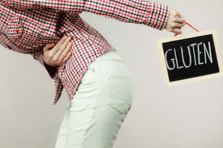 Wheat allergy problems concept. Woman having stomach cramps feeling very unwell holding board with...