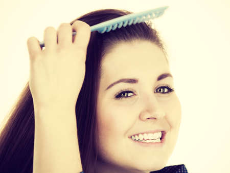 Woman combing her healthy hair using comb. Young latin female with beautiful natural brown straight...