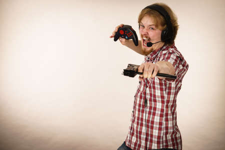 Nerd geek young adult man playing on the video console holding gun wearing headphones with microphone. Gaming gamers concept.の写真素材