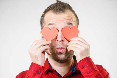 Adult funny man covering eyes with red hearts. Male blinded by love. Romance feelings valentines day conceptの写真素材